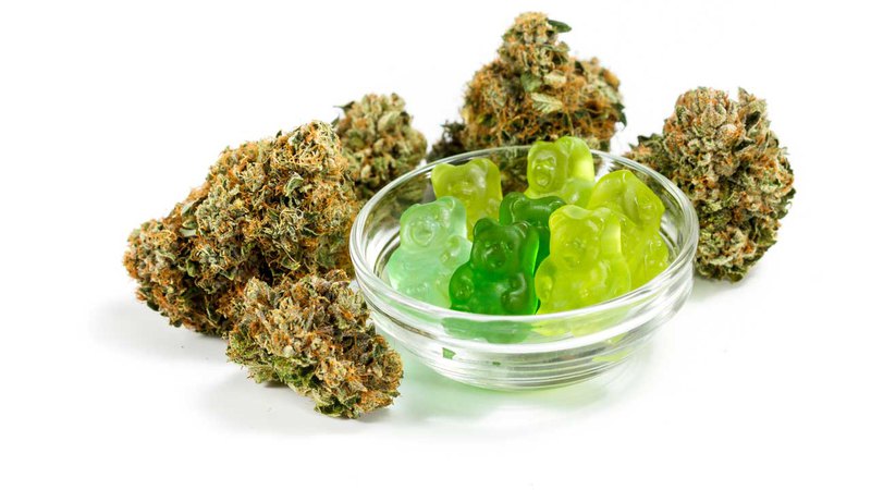 A bowl of green gummy bears is shown with cannabis flower. Are Delta-9 THC gummies legal?